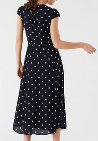 Granatowa sukienka w groszki z krótkimi rękawami, dopasowanym gorsetem i zwiewną spódnicą sięgającą poniżej kolan; wykonana z lekkiej tkaniny.