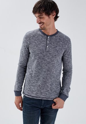 Grijze gemêleerde langemouwen henley shirt met een ronde hals, drie-knopen placket en geribbelde manchetten, gecombineerd met donkerblauwe jeans.