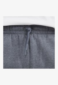 Pantalones de chándal grises con cintura ajustable mediante cordón gris y aglets de plástico. La textura es suave y de felpa, adecuada para un uso casual.