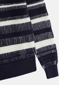 Pleteni pulover z mornarskimi in belimi črtami, rebrastimi manšeti in robom ter trikotno oznako na spodnji strani.