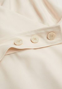 Gros plan d’un tissu beige avec trois boutons ronds assortis à quatre trous cousus sur une couture pliée.