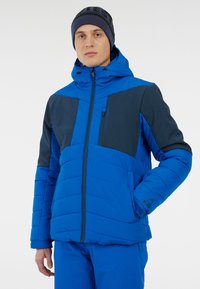 Modrá zateplená bunda s kapucí; obsahuje tmavě modré panely, přední zip a nastavitelné manžety, ukazuje prošívanou texturu a design.