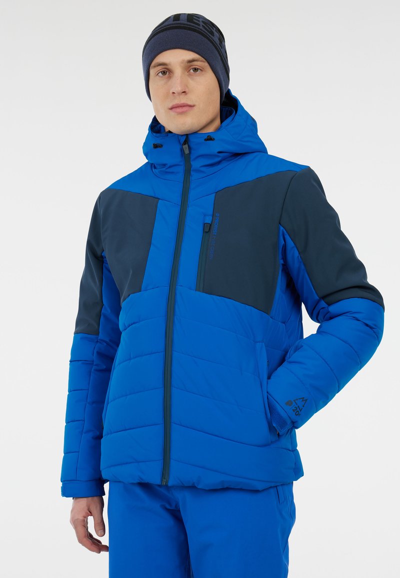 Modrá zateplená bunda s kapucí; obsahuje tmavě modré panely, přední zip a nastavitelné manžety, ukazuje prošívanou texturu a design.