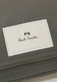 Szary worek z tkaniny o teksturowanym wzorze siatki, z białą metką z napisem "PS Paul Smith" w czarnym kursywie. Zszywane krawędzie.