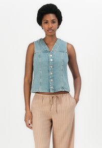Lys blå denim ermeløs vest med v-hals, frontknapper og en lett cropped passform, sammen med beige stribede bukser.