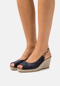 Navy suede wedge sandals with a peep-toe design and adjustable ankle strap. Textured jute-like wedge heel adds detail.