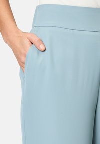 I pantaloni azzurri chiari presentano una trama liscia, una cintura larga e una tasca laterale. Il materiale appare morbido e scivola fluidamente.