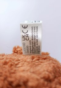 Orange plush fabric with soft texture; tag visible, showing care instructions and product details.
