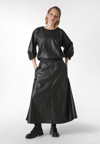 Conjunto de imitación de cuero negro que presenta una blusa de corte holgado con mangas abullonadas y una falda larga a juego, acentuada con una cinturilla elástica.