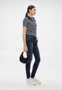 Prúžkované námornícke modro-biele polo tričko, tmavomodré úzke džínsy, krémové tenisky a malá čierna kabelka so zlatými doplnkami.