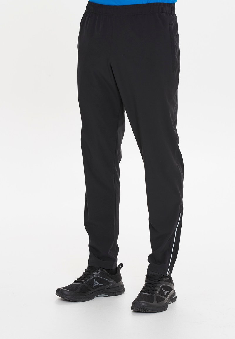 Zwarte sportbroek met een elastische tailleband, taps toelopende pasvorm, zijzakken en een reflecterende streep aan de zijkant. Gekocht met zwarte sneakers.