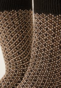 Bruna och svarta stickade strumpor med ett strukturerat mönster och inslag av guldfärgade trådar som ger en subtil skimrande effekt upptill.