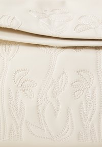 Pelle beige con motivi floreali in rilievo, caratterizzata da dettagli di cucitura intricati che creano una superficie testurizzata. Finitura liscia complessivamente.