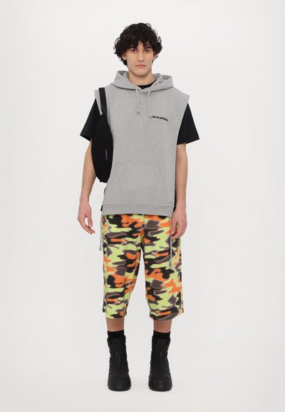 Grå ærmeløs hoodie over en sort t-shirt, parret med orange, grønne og sorte camo-shorts og sorte ankelstøvler. Sort crossbody taske.
