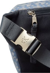 Borsa in tela blu con design a motivo, dotata di una tracolla scura e di una chiusura metallica con il logo "CK". Superficie testurizzata.