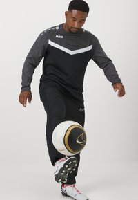 Completo sportivo nero e grigio con un design a zigzag, caratterizzato da un logo sul petto e un pallone da calcio con un motivo bianco e oro.