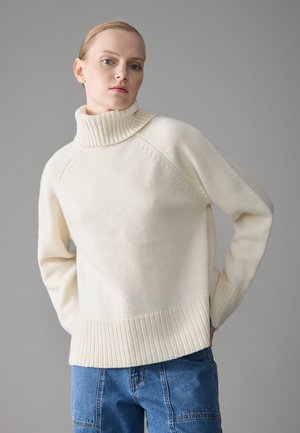 Kreemivärvi kudumistehnika krae-sweater, millel on soonik serv ja varrukad, pakkudes mugavat lõiget ja veidi tekstureeritud pinda. Kandi siniste teksadega.