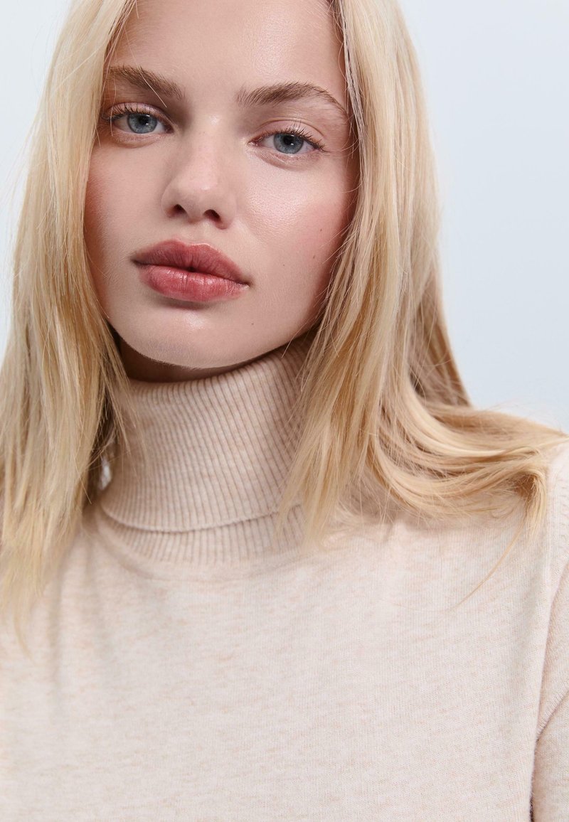 Helle beige gestrickte Rollkragenpullover mit Rippstruktur und hohem Kragen. Glattes Material mit einem feinen melierten Muster.