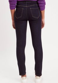 Jeans skinny bleu foncé avec une taille haute, dotés de deux poches arrière, de coutures contrastantes et d'un léger stretch. Associés à des baskets blanches.