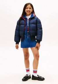 Ναυτικό πούφφερ μπουφάν με ριχτές μανσέτες, λευκό πουκάμισο με γιακά, τζιν φούστα και μαύρες loafers. Λευκές κάλτσες με κόκκινες και μαύρες ρίγες.