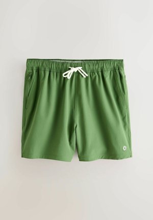 Green swim shorts made of soft fabric, featuring an elastic waistband with white drawstring, two side pockets, and a logo on the lower hem.