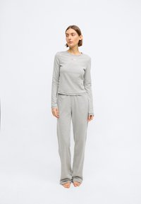 Siva dugouh rukav majica s malim logotipom i odgovarajuće sive hlače, izrađene od mekog materijala s glatkom teksturom i opuštenim krojem. Bez uzoraka ili naglasaka.