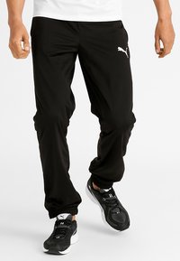 Svarta träningsbyxor med elastisk midja och avslutade anklar. Har sidofickor och en vit Puma-logga på vänster lår.