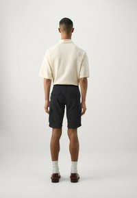 Polo shirt color crema a maniche corte con una vestibilità rilassata, abbinato a pantaloni cargo scuri con tasche laterali e un tessuto testurizzato.
