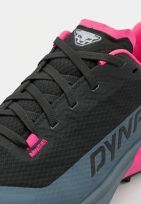 Svart og grå idrettssko med strukturert overdel, rosa detaljer, fremtredende snøresystem og en logo på tungen og siden.