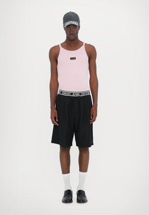 Rosa ribbet tanktopp med en logo-patch, svarte plisserte shorts med merkebånd, hvite sokker, og svarte slip-on sko.