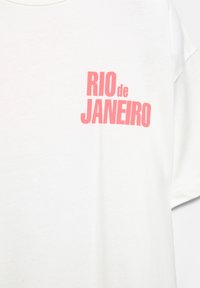 Bílá bavlněná tričko s velkým růžovým textem, který zní "RIO de JANEIRO." Krátké rukávy a kulatý výstřih. Hladká textura.