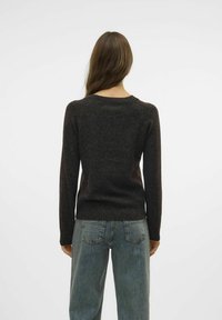 Maglione grigio scuro con scollatura rotonda, maniche lunghe e finitura testurizzata. Abbinato a jeans chiari a vita alta.