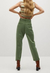 Pantalon vert taille haute avec une coupe décontractée, doté de deux poches arrière et de détails de plis, associé à des bottines brunes.