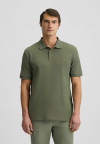 Olivgrünes Poloshirt mit kurzen Ärmeln, klassischem Kragen, Knopfleiste mit drei Knöpfen und dezentem Logo auf der Brust. Glattes Baumwollmischgewebe.