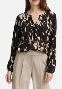 Blouse à manches longues noire et marron à motifs, avec une coupe décontractée, un col en V et un détail de bouton, associée à un pantalon taille haute beige.