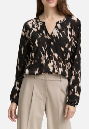 Blouse à manches longues noire et marron à motifs, avec une coupe décontractée, un col en V et un détail de bouton, associée à un pantalon taille haute beige.