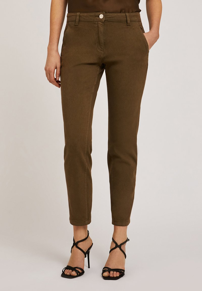 Pantalones marrones ajustados de una tela suave y lisa con cremallera y cierre de botón. Combinados con sandalias negras de tacón con tiras entrecruzadas.