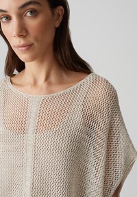Haut léger en tricot ouvert beige, avec un large décolleté et des manches amples. Le motif texturé offre une respirabilité et une coupe décontractée.