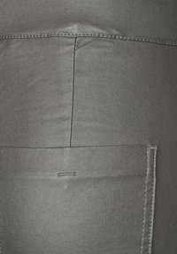 Grå denimtyg med en slät textur; har bakfickor och en sydd sömdekor. Tyget visar lätt veck.