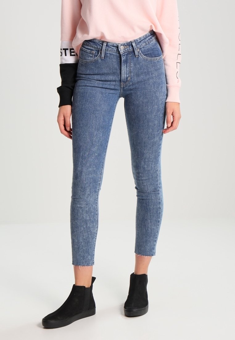 Jeans de mezclilla azul ajustados con cintura alta, dobladillo deshilachado y un lavado desgastado, combinados con botas de tobillo negras para crear contraste.