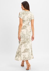 Maxikleid aus cremefarbenem Stoff mit grünem tropischen Druck. Hat kurze Ärmel, einen Taillengürtel und einen fließenden Rock. Wird mit beigen Absätzen getragen.