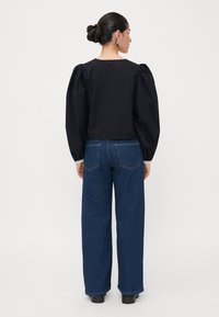 Black cropped top with puffed sleeves, paired with high-waisted blue denim wide-leg jeans. Simple design, minimal detailing, and a relaxed fit.
