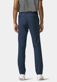 Marineblauwe broek met een op maat gemaakt fit, twee achterzakken, geweven riem en minimale stikdetails, gecombineerd met witte sportschoenen.