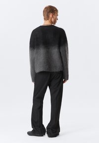 Un pull flou, en dégradé de gris, au fit oversize avec un col rond ; associé à un pantalon noir à rayures et à des chaussures texturées.