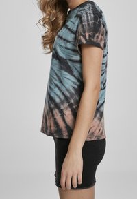 T-shirt med tie-dye mönster i turkos, svart och persika. Tillverkad av bomull, med korta ärmar och en avslappnad passform.