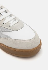 Ljusgrå sneakers med mocka- och lädermaterial, rundad tå, vita snören och en sula i gummimaterial. Texturerade detaljer på sidorna.