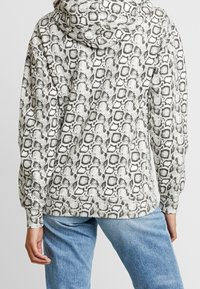 Mikina s kapucí v krémovém a šedém hadím vzoru, s volným střihem, žebrovanými manžetami a klokaní kapsou.