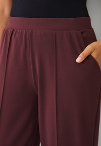 Pantalones burdeos de pierna ancha con una textura suave, que presentan un diseño plisado y bolsillos laterales para mayor funcionalidad.