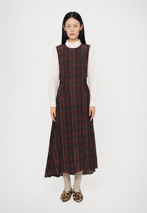 Robe longue à carreaux en rouge foncé et noir avec une taille cintrée, présentant un col haut et des poches latérales ; portée sur une chemise blanche à col.