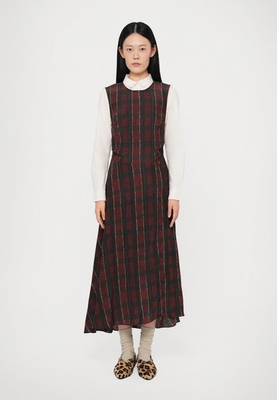 Robe longue à carreaux en rouge foncé et noir avec une taille cintrée, présentant un col haut et des poches latérales ; portée sur une chemise blanche à col.